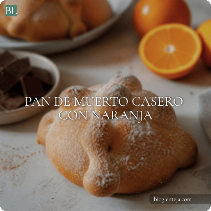 Pan de muerto casero cubierto con azúcar sobre una mesa, acompañado de naranja y chocolate caliente.
